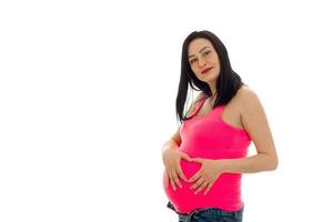 cute pregnant girl with dark hair touching her big belly and looking at the camera isolated on white background photo