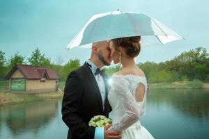 joven pareja casada se besa bajo un paraguas foto