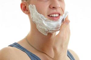 young guy smiles and deals the hand shaving foam on beard close-up photo