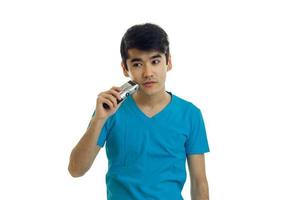 cute young guy with thick black hair stands straight and shaves his beard photo