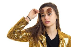 close up portrait of pretty brunette woman in round sunglasses and golden jacket looking at the camera photo