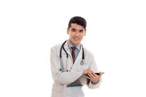 young perky doctor keeps a stethoscope on the shoulders and board in hand isolated on white background photo