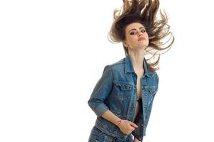 una joven hermosa con chaqueta de jeans se para frente a la cámara y su cabello vuela por el aire foto