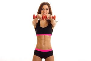 a svelte young fitness girl stands directly in sports shorts and top and stretch your arms forward with dumbbells photo