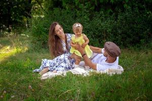 feliz familia joven juega con su hijita en el prado grren foto