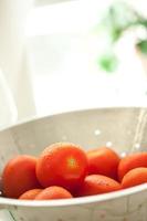 tomates roma frescos y vibrantes en colador con gotas de agua foto