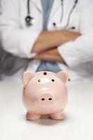 Doctor with Folded Arms Behind Piggy Bank photo