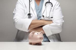 Doctor with Folded Arms Behind Piggy Bank photo