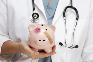 Doctor Holding Piggy Bank with Bruised Eye and Bandage photo