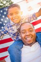 padre afroamericano e hijo de raza mixta piggy back con bandera americana foto