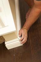 Contractor Fitting New Baseboard to Wall and New Laminate Flooring photo