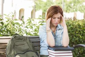 Female Student Outside with Headache Sitting with Books and Backpack photo