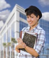 estudiante de raza mixta sosteniendo libros frente al edificio foto