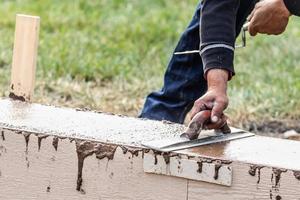 Construction Worker Using Wood Trowel On Wet Cement Forming Coping Around New Pool photo