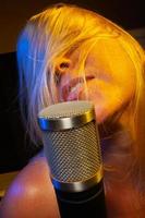 Female vocalist under gelled lighting sings with passion into condenser microphone. photo