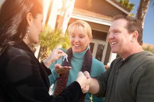 Hispanic Female Real Estate Agent Handing Over New House Keys to Happy Couple In Front of House photo