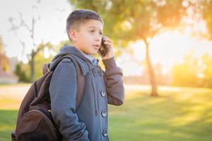 joven hispano caminando al aire libre con mochila hablando por teléfono celular foto