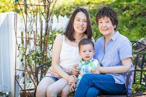 Chinese Grandmother, Daughter and Mixed Race Child Sit on Bench Outdoors photo