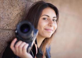 joven fotógrafa étnica adulta contra la pared sosteniendo la cámara. foto