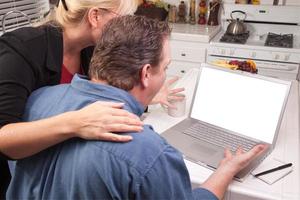 pareja en la cocina usando una laptop con pantalla en blanco foto