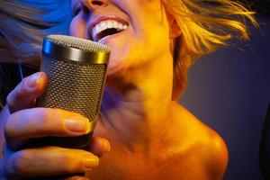 Female vocalist under gelled lighting sings with passion into condenser microphone. photo