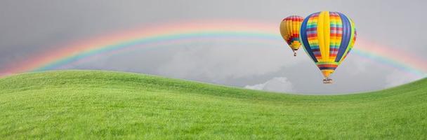 los globos de aire caliente se desplazan sobre el campo de hierba con un arco iris en el cielo. foto