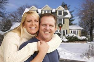 pareja frente a una hermosa casa con nieve en el suelo foto