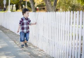 Joven muchacho de raza mixta caminando con bastón a lo largo de valla blanca foto