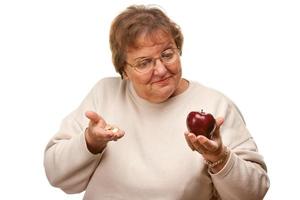 Confused Senior Woman Holding Apple and Vitamins photo