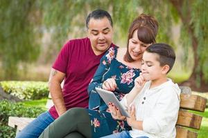 Caucasian Mother and Hispanic Father Using Computer Tablet With Mixed Race Son Outdoors photo