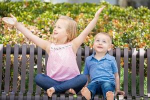 hermana joven y hermano divirtiéndose en el banco en el parque foto