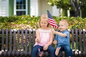 Young Sister and Brother Comparing Each Others American Flag Size On The Bench At The Park photo
