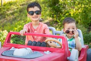 Jóvenes hermanos chinos y caucásicos de raza mixta con gafas de sol jugando en un coche de juguete foto