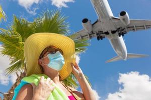chica con toalla, sombrero, gafas de sol y mascarilla debajo de una palmera y un avión foto