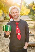 apuesto joven caucásico festivo sosteniendo un regalo de navidad al aire libre foto