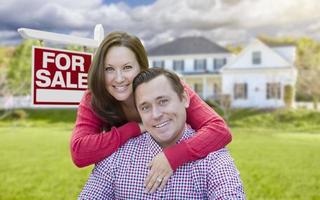 pareja feliz frente a la casa y el cartel de venta foto