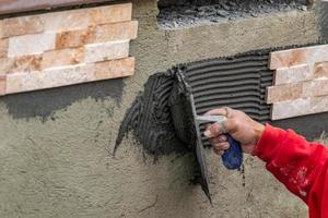 trabajador instalando cemento de baldosas de pared con paleta y baldosas en el sitio de construcción foto