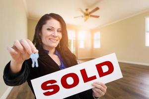Hispanic Woman With House Keys and Sold Real Estate Sign In Empty Room of House photo