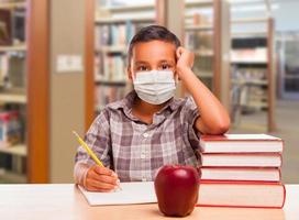 Hispanic Boy Wearing Face mask with Books, Apple, Pencil and Paper at Library photo