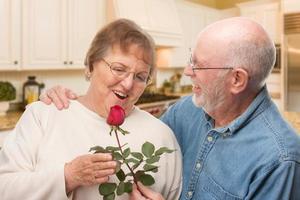 Happy Senior Adult Man Giving Red Rose to His Wife Inside Kitchen. photo