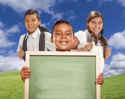niños y niñas hispanos en el campo sosteniendo una pizarra en blanco foto