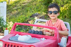 joven chino de raza mixta y caucásico con gafas de sol jugando en un coche de juguete foto