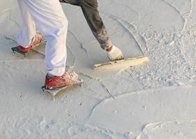 trabajador que usa zapatos con púas alisando el yeso húmedo de la piscina con una paleta foto