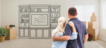 Couple Inside Empty Room with Moving Boxes Facing Entertainment Unit Drawing on Wall photo