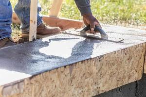 Construction Worker Using Wood Trowel On Wet Cement Forming Coping Around New Pool photo