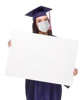 mujer que se gradúa con mascarilla médica y toga y birrete sosteniendo una cartulina en blanco aislada en un fondo blanco foto