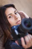 joven fotógrafa étnica adulta contra la pared sosteniendo la cámara. foto