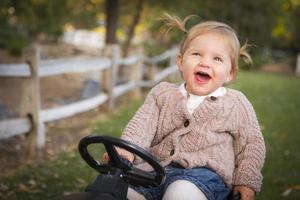 niño pequeño riendo y jugando en un tractor de juguete afuera foto