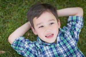 Thoughtful Mixed Race Chinese and Caucasian Young Boy Relaxing On His Back Outside On The Grass photo