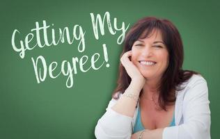 Getting My Degree Written On Green Chalkboard Behind Smiling Middle Aged Woman photo
